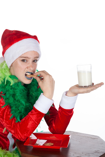 Closeup portrait of young girl wearing red santa clause hat like grinch snarling with biscuit in mouth, isolated on white background. Cheeky human emotion facial expression