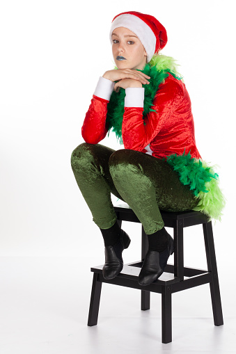 Sitting young girl wearing red santa clause hat like a grinch Grinch chin on hands looking bored, isolated on white background. Bored human emotion expression