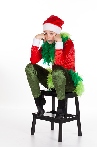 Sitting young girl wearing red santa clause hat like a grinch hands to face in sad and lonely expressive pose, isolated on white background. Negative sad human emotions