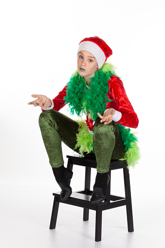 Sitting young girl wearing red santa clause hat like a grinch holding hands out in 'yeah what' pose, isolated on white background. Questioning concept of human emotions