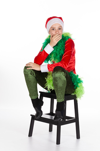 Young girl wearing red santa clause hat like a grinch hand covering mouth in shock expression, isolated on white background. Shocked human emotion facial expression