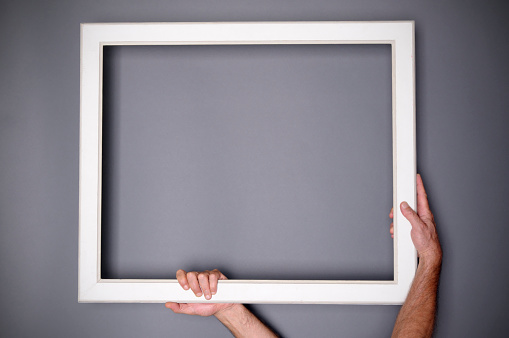 Hands holding blank frame on grey background. Copy Space.