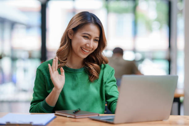 Beautiful young Asian woman college student is video chatting with her classmates using laptop, smiling faces and gestures happily studying.