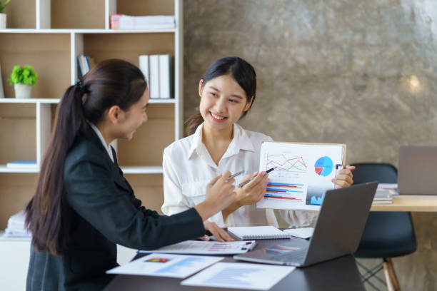 istock Two professional young Asian business women discuss work, graph, chart using laptop computer for office work. 1483767455