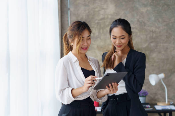 istock Two beautiful Asian business women stand and talk about work using a tablet in the office. 1483767688