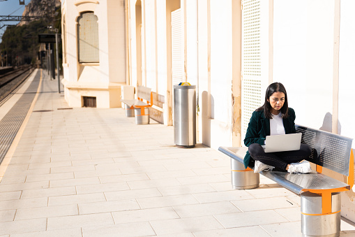 Totally alone woman works with laptop at train station sitting on bench