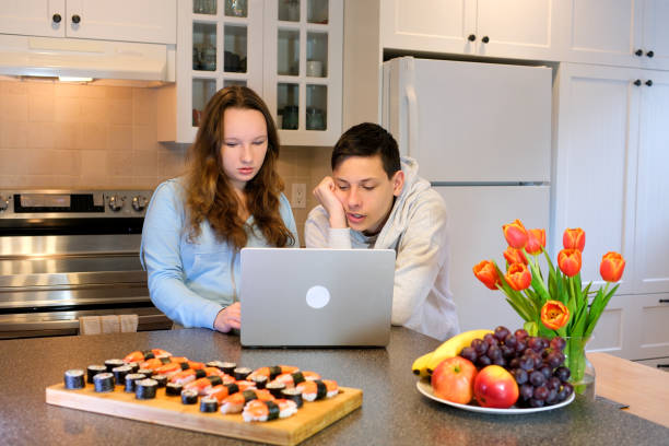 посмотреть на ноутбук наклониться сосредоточенно подумать посмотреть подростки делают домашнее задание на кухне заказали суши встретить� - teenager 14 15 years 13 14 years cheerful стоковые фото и изображения