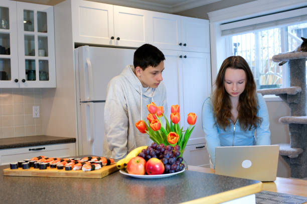 mirar la computadora portátil inclinarse sobre enfocado pensar mirar adolescentes haciendo la tarea en la cocina ordenado sushi reunirse después de la escuela primera cita ver película pasar tiempo juntos niño niña 13 14 15 años - 13 14 years teenager teenagers only female fotografías e imágenes de stock