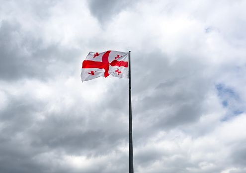 The national flag of Georgia flutters against the backdrop of cloudy sky.