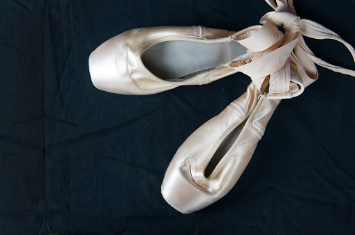A pair of white, and a pair of pink color pointe shoes on a patched white background.