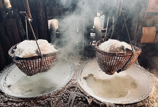 Beautiful smoke, sunlight shines down around ancient salt pits and bamboo basket. Ancient method of boiling brine into pure salt in Bo Kluea, Nan, Thailand.