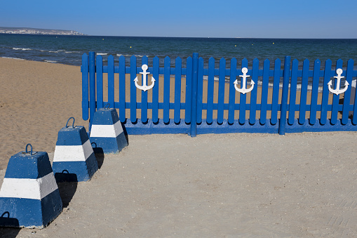 Blue wooden fence with white anchor. Mediterranean sea in the background.