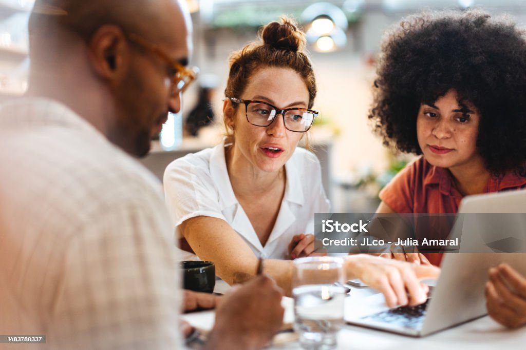 Business women having a discussion with a client over a business lunch Business women having a work lunch in a café, exchanging ideas and discussing their projects with a client. Young business team using a laptop as they sit around a coffee table. Meeting Stock Photo