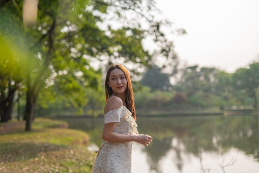 Attractive red-haired girl in a white lace dress walks in a green summer park.