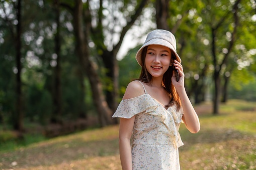 Half body shot of a young asian woman using her mobile phone in a park. Woman smiling happily while talking on the phone.