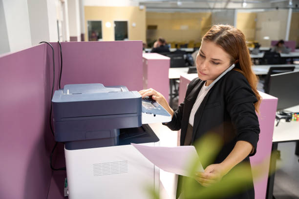 Stock photo showing close-up view of an unrecognisable man sitting in an office chair replacing the telephone receiver on a landline telephone base unit as he works in an office environment.