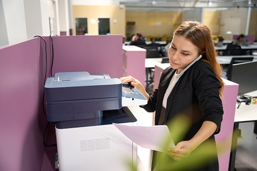 Female standing near the printer and checking the printed documentation in the business center