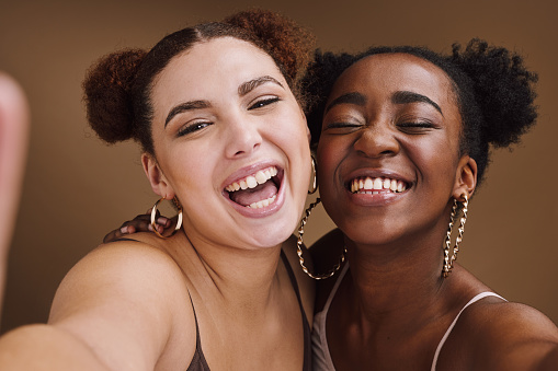 Beauty, friends and smile with selfie of black women for social media, skincare and fashion. Happy, bonding and picture with portrait of girl for funny, laughing and comic in brown background studio