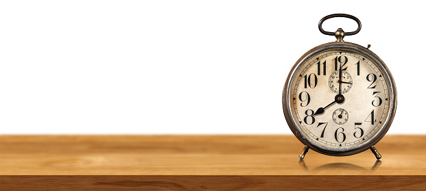 Closeup of an old alarm clock on a wooden table isolated on white background with copy space. Eight o'clock, Italy.