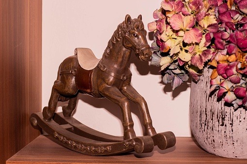 A vibrant vase of assorted flowers near a wooden rocking horse on a rustic shelf
