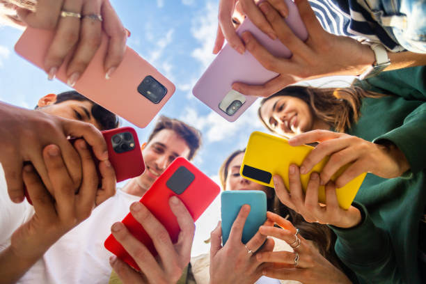 grupo joven de personas que usan un dispositivo de teléfono móvil de pie en círculo al aire libre - adicto grupo de jóvenes amigos usando teléfonos móviles fotografías e imágenes de stock