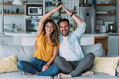 Happy couple making roof figure with their arms in the living room.