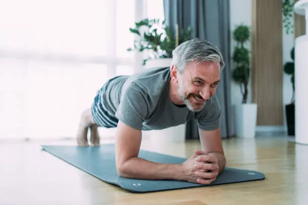 Shot of a confident mature man doing plank position while exercising on the floor in the living room at home.
