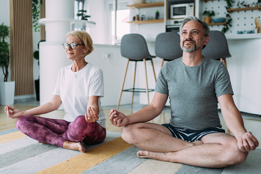 Beautiful mature couple sitting on the floor and practicing yoga.