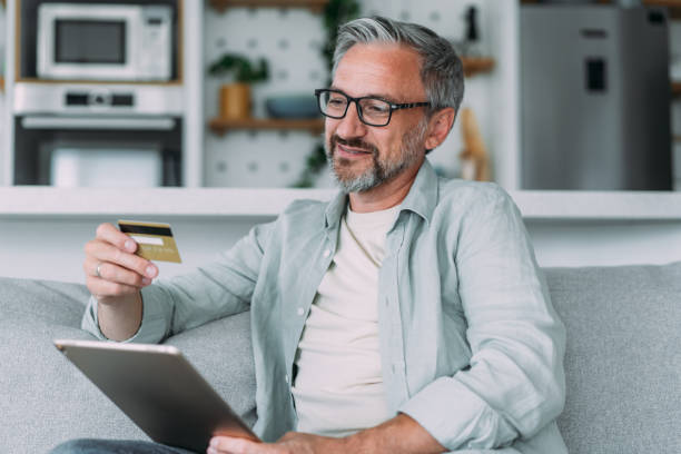 istock Man sitting on the sofa at home and using tablet for online shopping. 1483802402