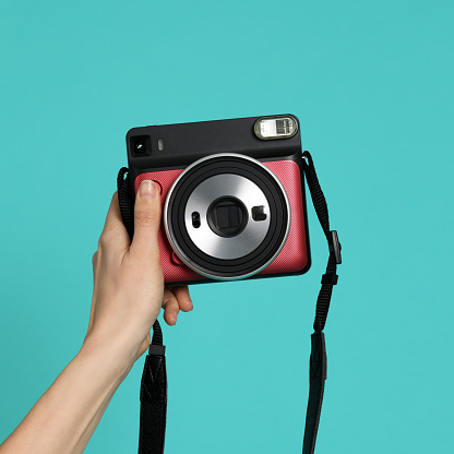 Hand with instant camera on mint background