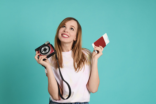 Young pretty woman with camera and passport on mint background