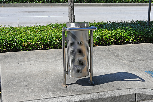 Stainless steel garbage bin on a concrete footpath or sidewalk