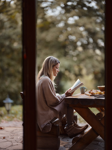 Young woman reading a book while relaxing on a patio in autumn day. Copy space. Photographed in medium format.