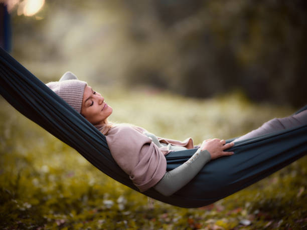 Smiling woman relaxing in hammock at the park. Young smiling woman relaxing in hammock with her eyes closed during autumn day in nature. Copy space. Photographed in medium format. hammock relaxation women front or back yard stock pictures, royalty-free photos & images