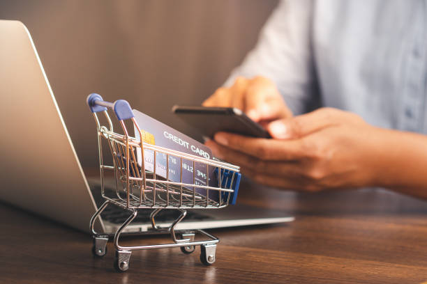 istock A mini shopping trolley on a wooden table with a man using a smartphone blur the background while sitting in the office. 1483809338