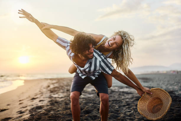 istock Cheerful couple having fun while piggybacking on the beach at sunset. 1483811147