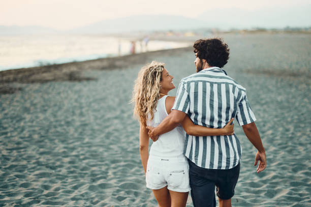 istock Back view of happy couple talking while walking embraced on the beach. 1483811997