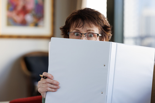 Senior woman looking over the top of a white folder.