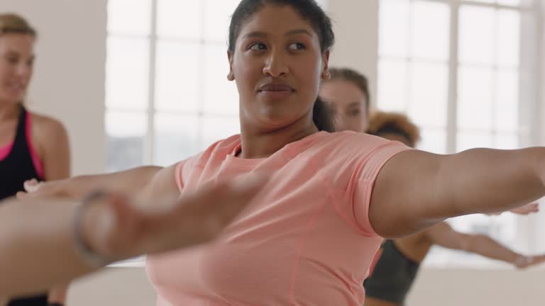 yoga class young overweight mixed race woman practicing warrior pose enjoying healthy lifestyle commitment fitness instructor teaching diverse group meditation in studio