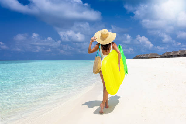 istock A woman in a white bathing suit holding a floatie and hat walks down a tropical beach 1483815119
