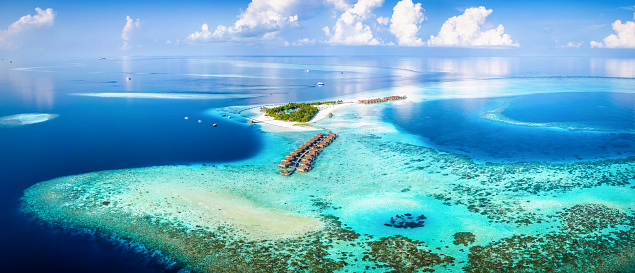 Panoramic aerial view of a turquoise coral reef and lagoon with a tropical paradise island and calm sea at the Maldives, Indian Ocean