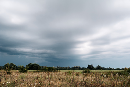 Gray wave rain clouds in front of a field, village