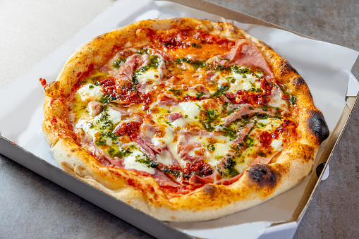Fresh round baked Ham & Cheese pizza in opened delivery box, with mozzarella cheese and ham