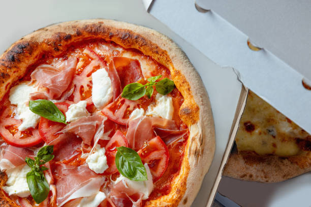 istock Pizza with prosciutto, tomato and mozzarella topping in open delivery box 1483819139