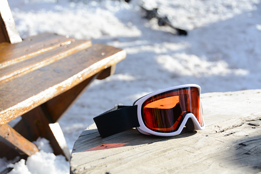 Skiing glasses with orange glass on a wooden table after skiing. A break after the skiing. Tea time after skiing.
