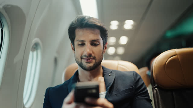 Businessman passenger using mobile phone while travelling by airplane.