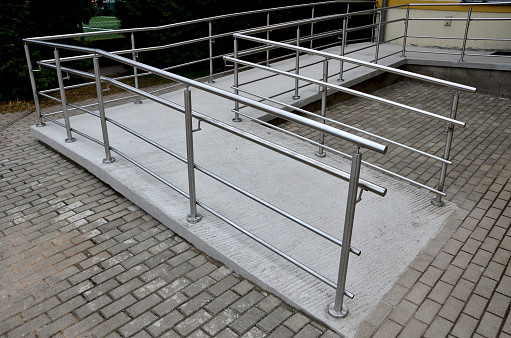 the curved ramp at the entrance to the building is suitable for wheelchair access and supply to the building. stainless steel railing, concrete surface, handrail, immobile
