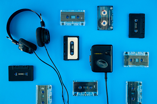 High angle view of an arrangement of audio cassettes, headphones and portable cassette player on a colorful background.