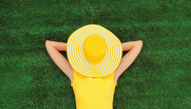 Happy relaxing girl with straw hat covering her face lies on green grass in summer park, top view stock photo