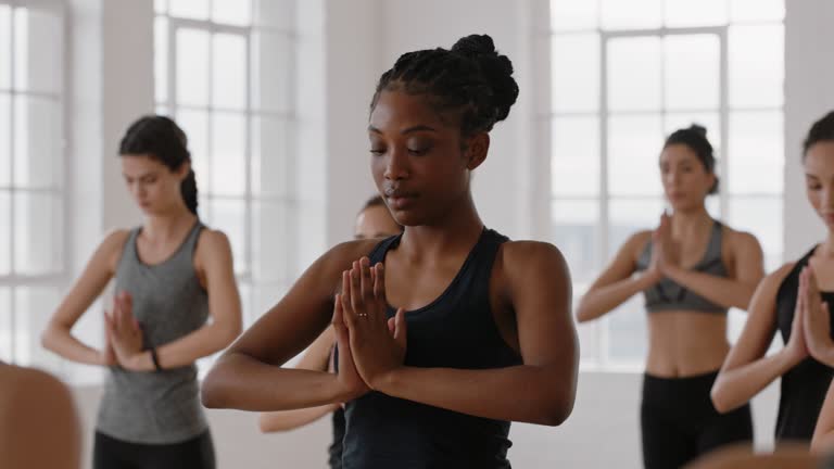 beautiful african american yoga woman practicing traingle pose meditation with group of multiracial women enjoying healthy lifestyle exercising in fitness studio at sunrise